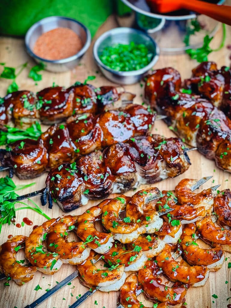 skewers with shrimp and chicken with bacon on a cutting board with parsley
