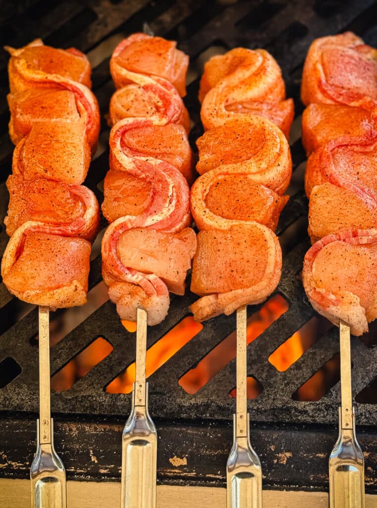 chicken and bacon skewers on a grill over hot coals