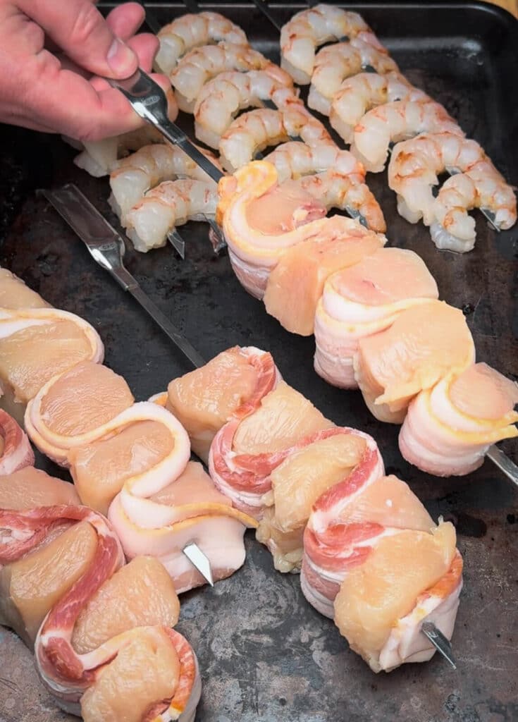 uncooked chicken and bacon skewers on a baking sheet