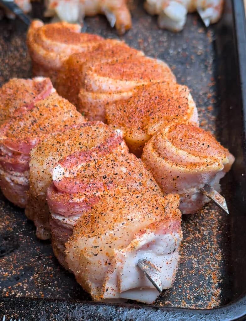 seasoned chicken and bacon skewers on a baking sheet