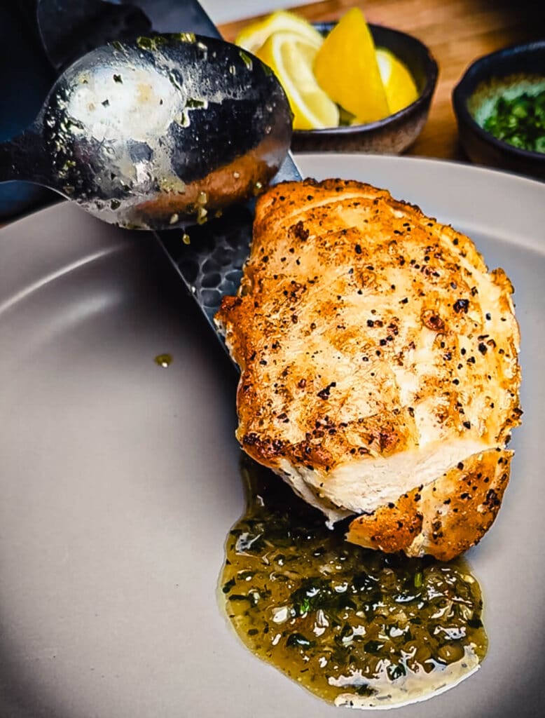 seared chicken being placed on a plate with pan sauce