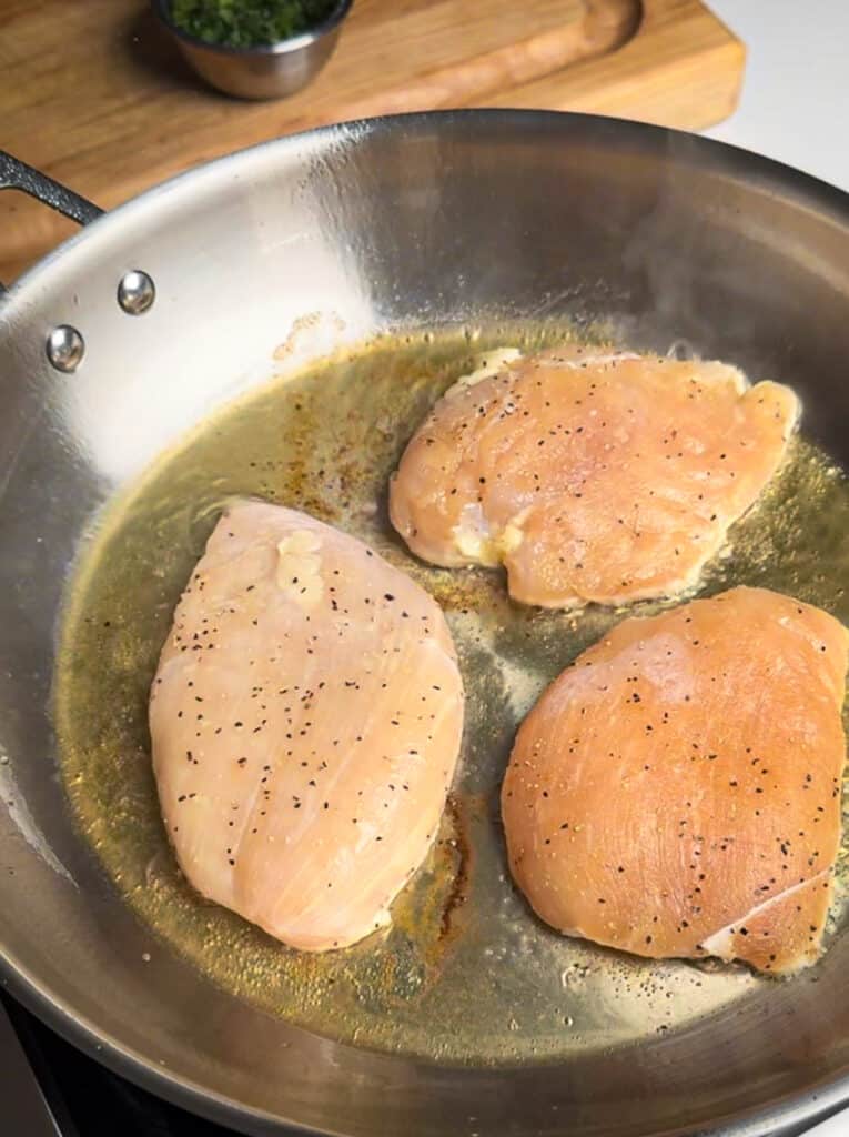 chicken searing in stainless steel pan