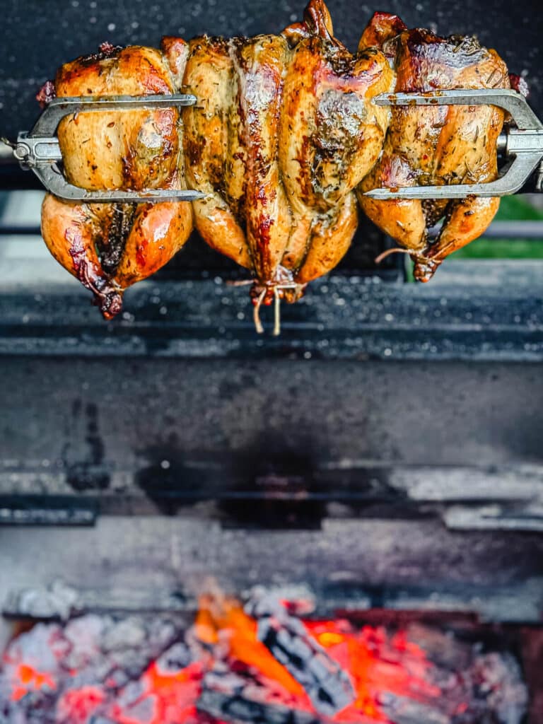 Cooked Cornish hens over a bed of hot coals on a rotisserie spit
