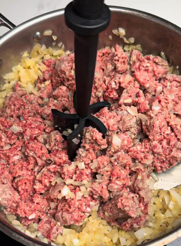 masher being used to break up ground beef in a pan