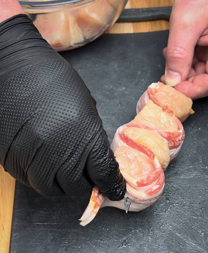 bacon being laced onto a skewer with chunks of chicken
