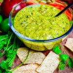 Glass bowl filled with roasted tomatillo salsa and a black spoon with tortilla chips
