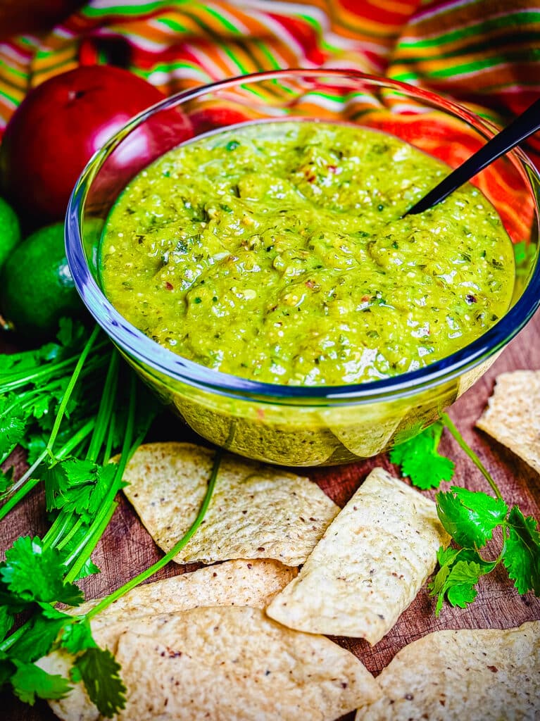 Glass bowl filled with roasted tomatillo salsa and a black spoon with tortilla chips