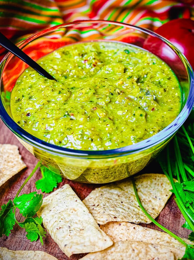 tortilla chips laying next to a bowl of roasted tomatillo salsa