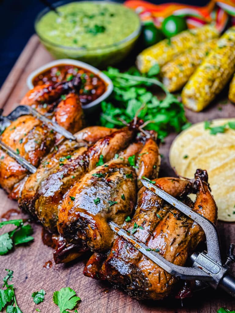 rotisserie grilled Cornish hens on a cutting board with corn and beans