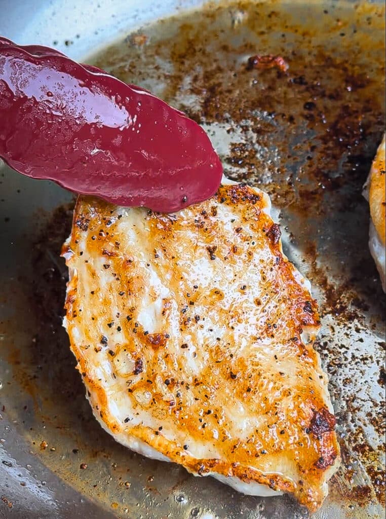 chicken breast being flipped with tongs in a pan