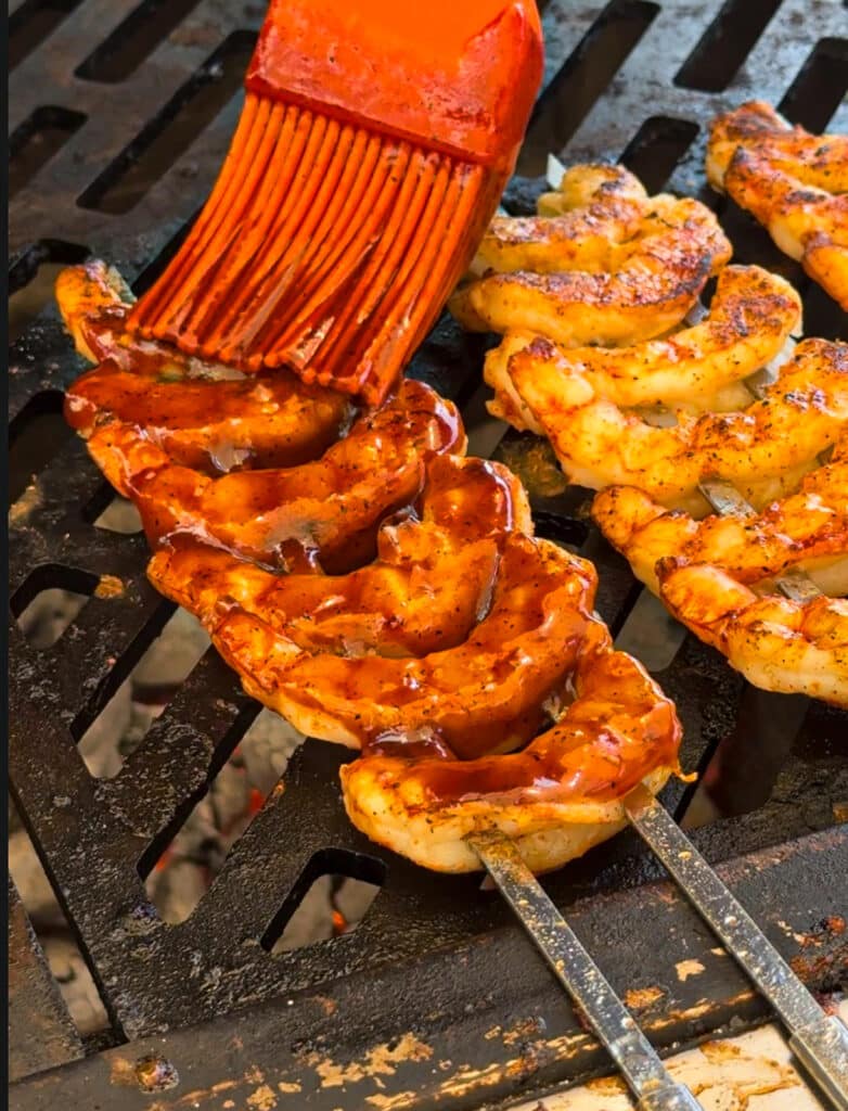 sauce being applied to grilled shrimp on a grill grate