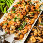 white platter with sweet chili shrimp on skewers garnished with parsley with green snap peas in the background