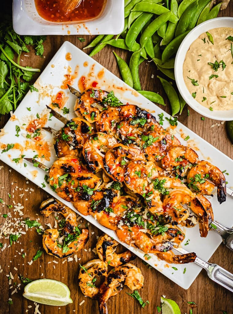 overhead shot of charred shrimp on a platter with dipping sauce and lime wedges