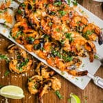 platter full of sweet chili shrimp on skewers with lime wedges