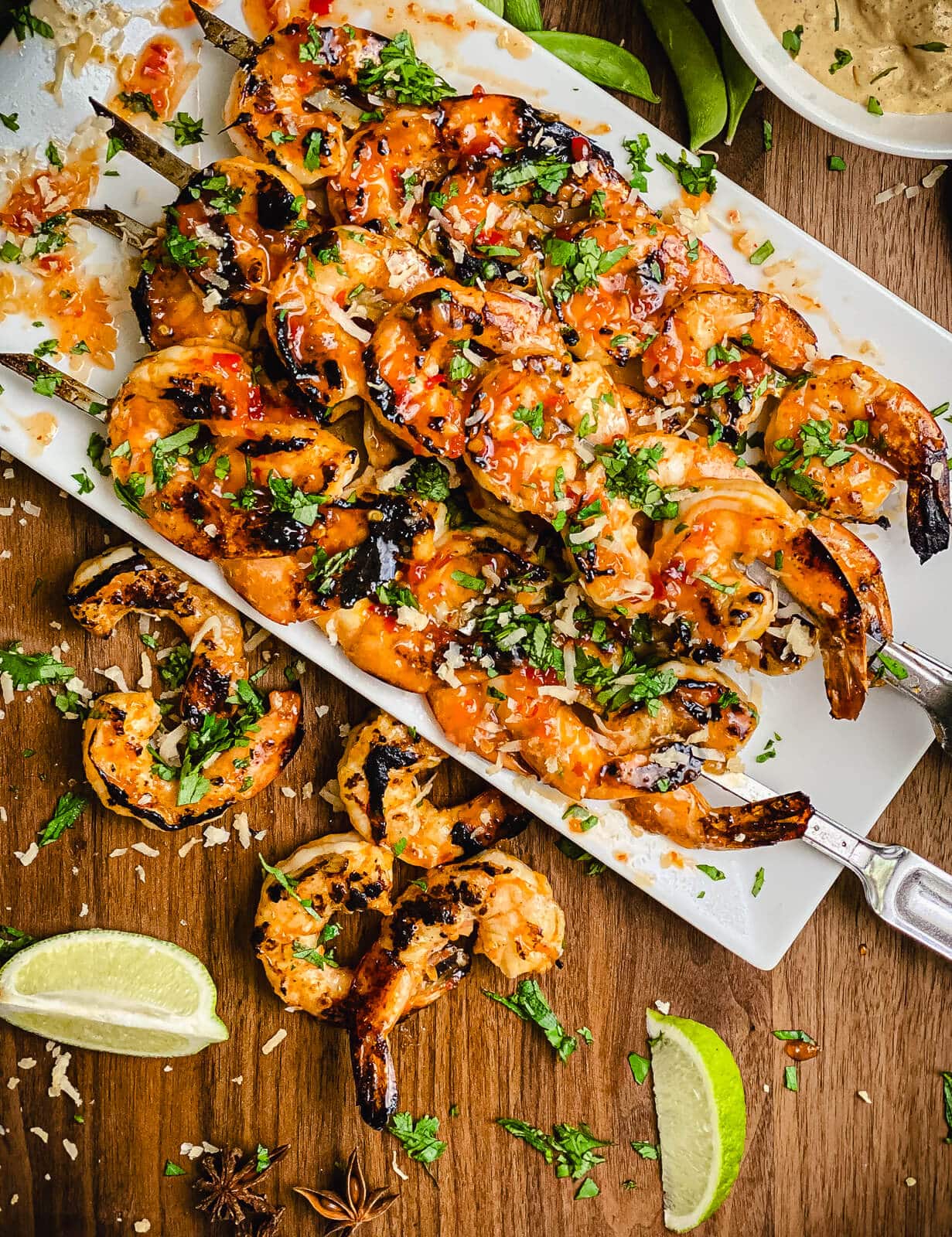 platter full of sweet chili shrimp on skewers with lime wedges
