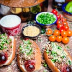 taco dogs wrapped in bacon on a platter with condiments and chili