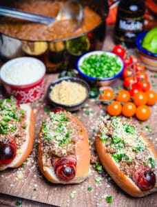 taco dogs wrapped in bacon on a platter with condiments and chili