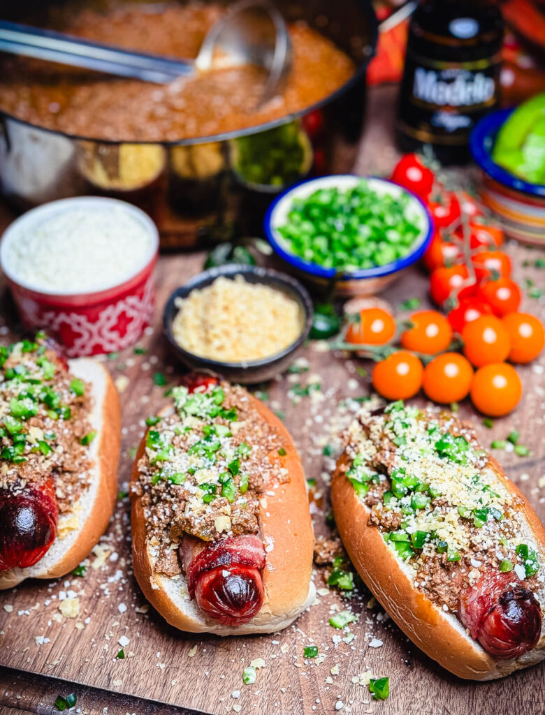 taco dogs wrapped in bacon on a platter with condiments and chili