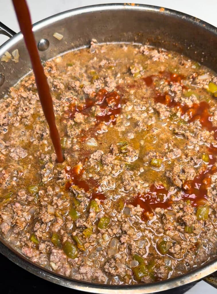 taco sauce being added to taco chili in a pan
