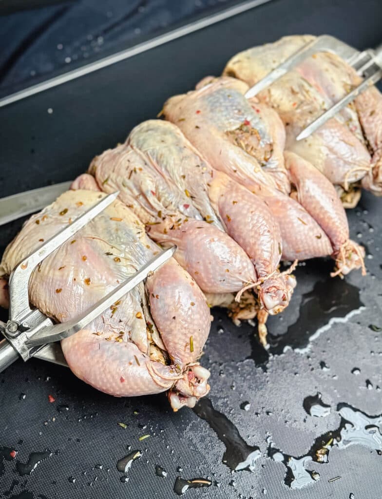 uncooked seasoned Cornish hens on a rotisserie spit