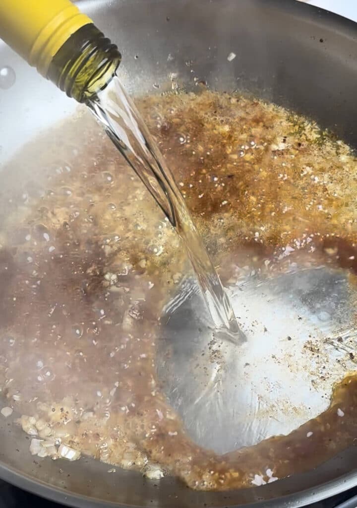 white wine being added to deglaze a stainless steel pan
