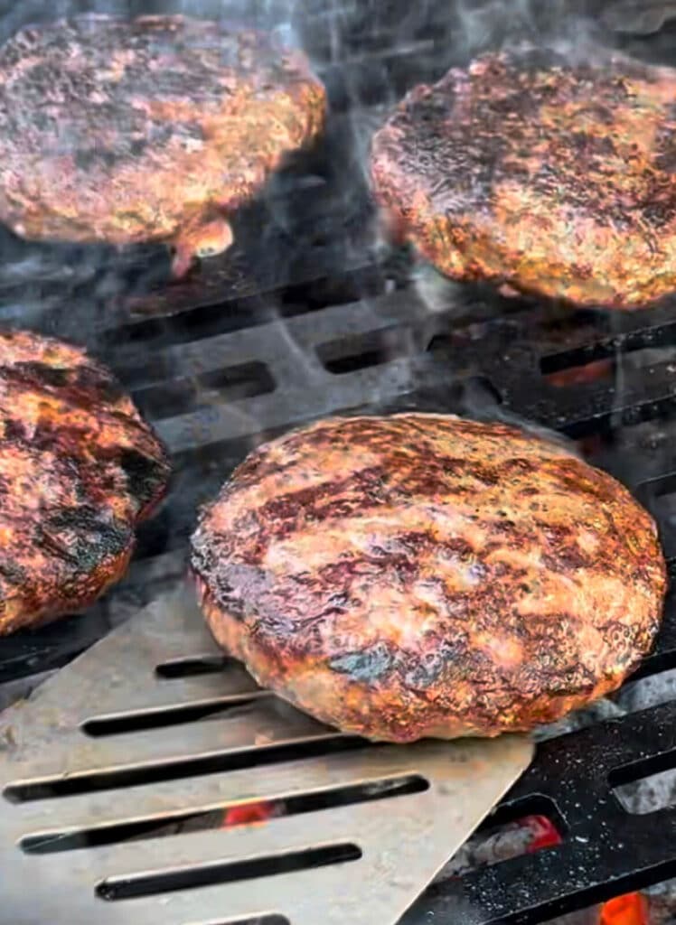 burger patty being grilled over hot coals