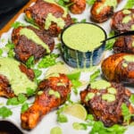 peruvian grilled chicken on a platter with green sauce on the chicken
