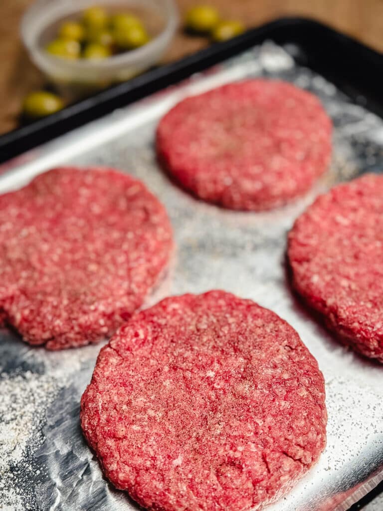 ground beef patties seasoned with salt and pepper on a baking sheet