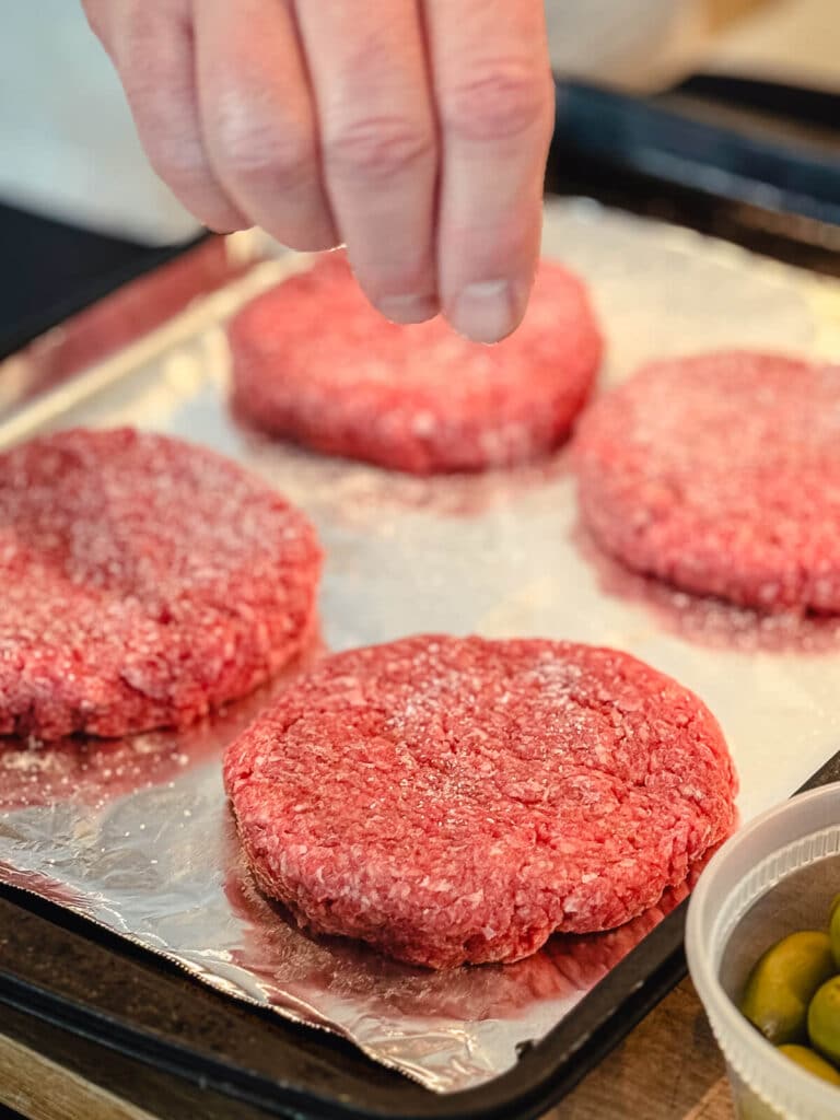 hand sprinkling salt on a ground beef patty