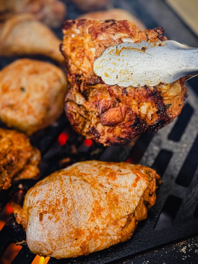 chicken thigh in a tong being turned over a grill and hot coals