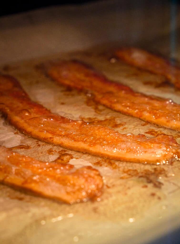 bacon sizzling on a baking sheet in an oven