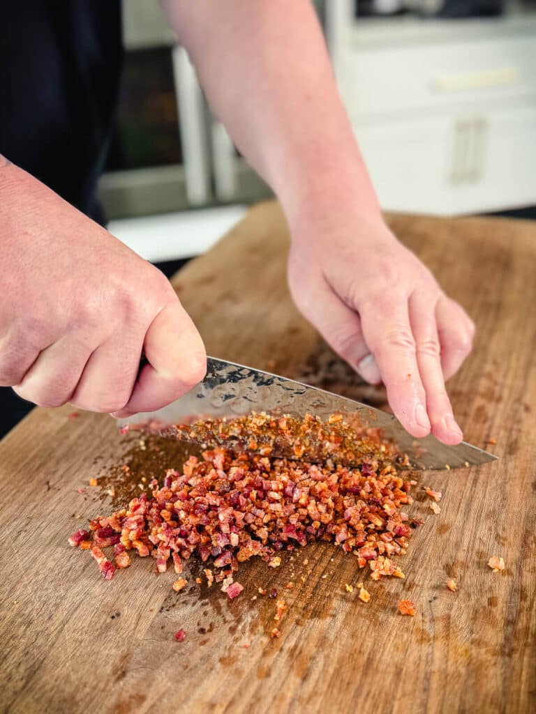 sharp knife chopping up crispy bacon on a cutting board