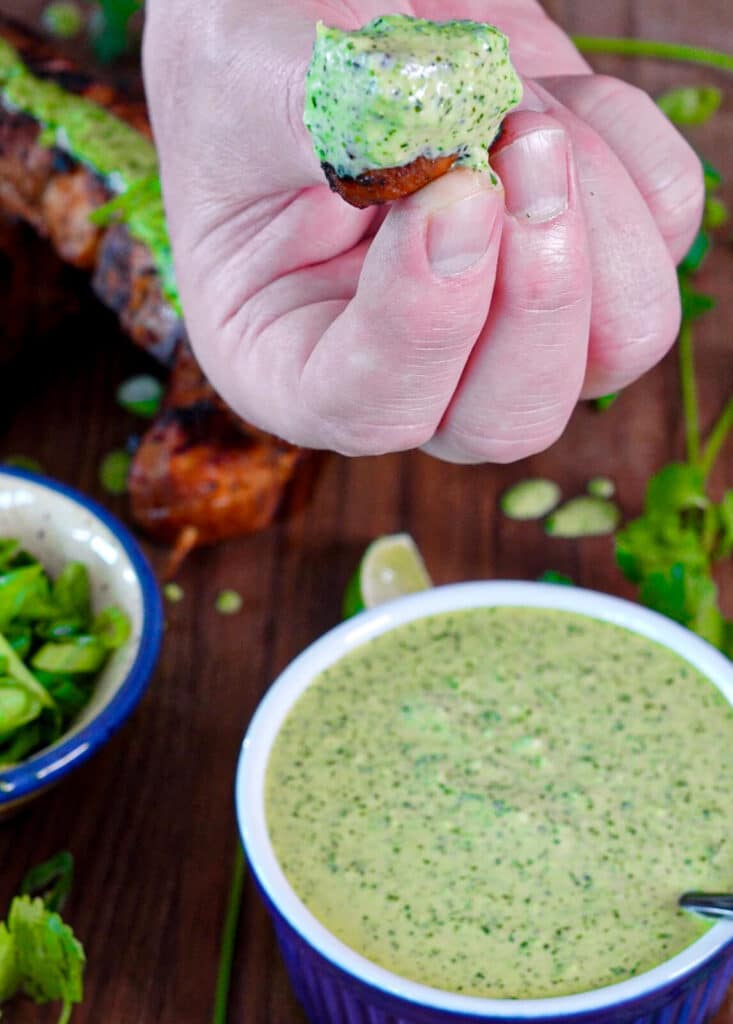 fingers holding a piece of Peruvian chicken dipped in green sauce