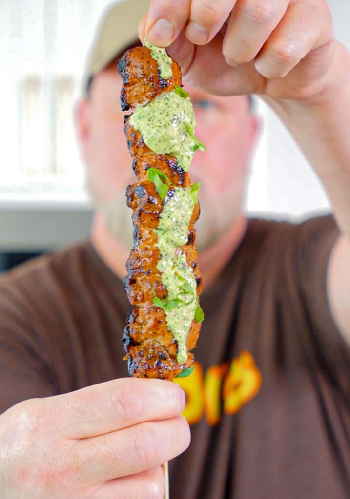 two hands holding a Peruvian chicken breast skewer with green sauce