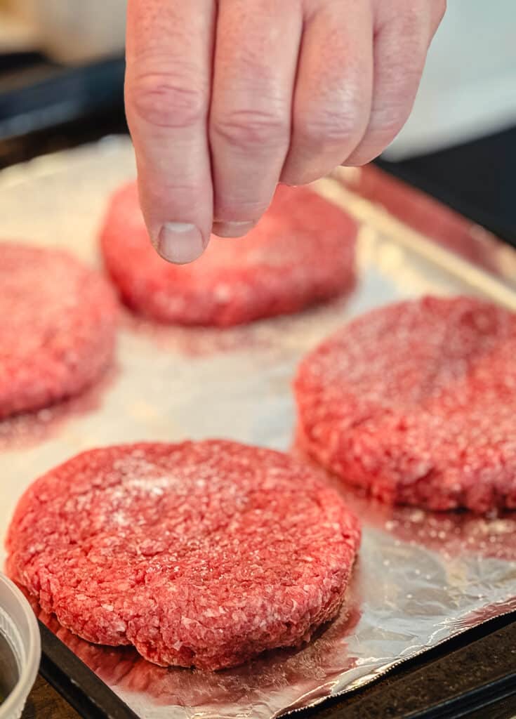 salt being sprinkled onto a ground beef patty