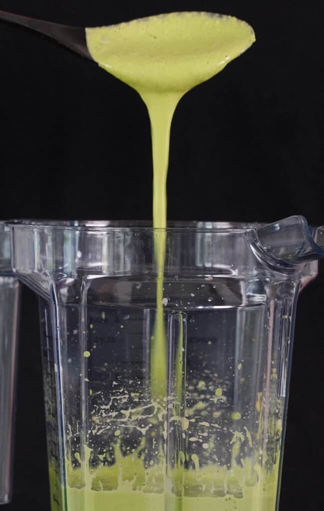 aji verde sauce being drizzled from a spoon over a blender container