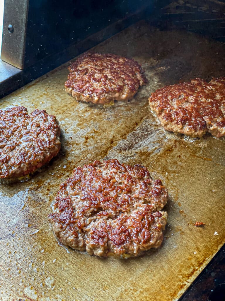 ground beef burger patties being seared on a flat top griddle