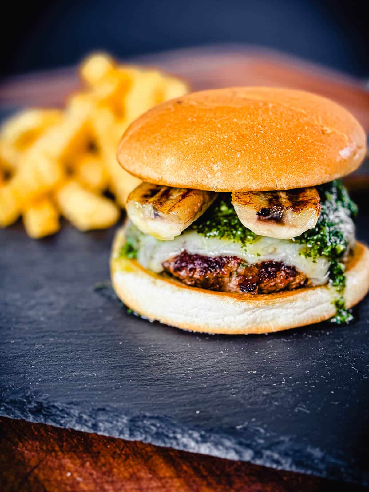 Columbain burger with grilled bananas on a black slate tile with french fries