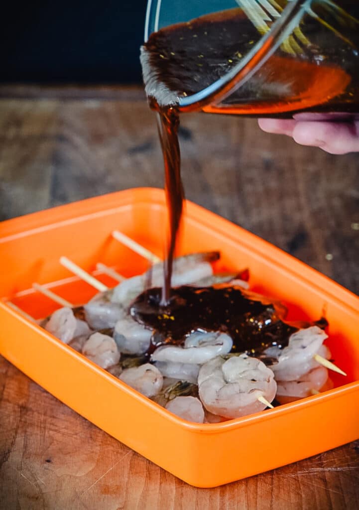 marinade being poured over top of shrimp skewers
