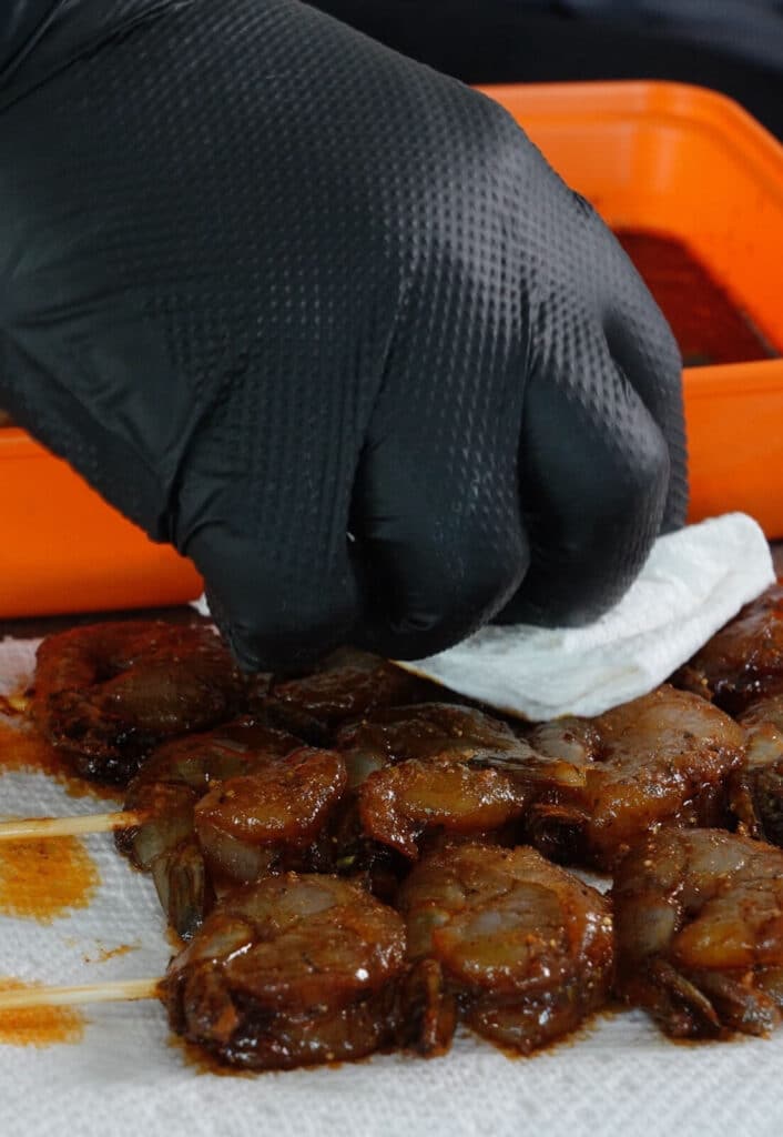paper towel being used to dab off marinade from shrimp skewers