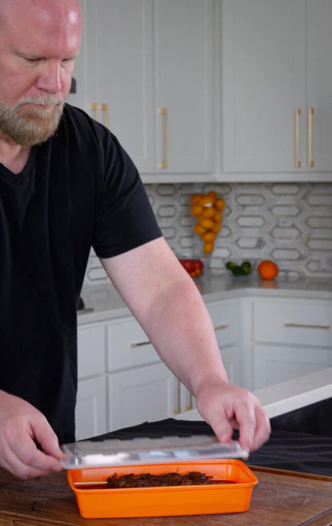 chef in a kitchen placing a lid on a container of marinating shrimp.