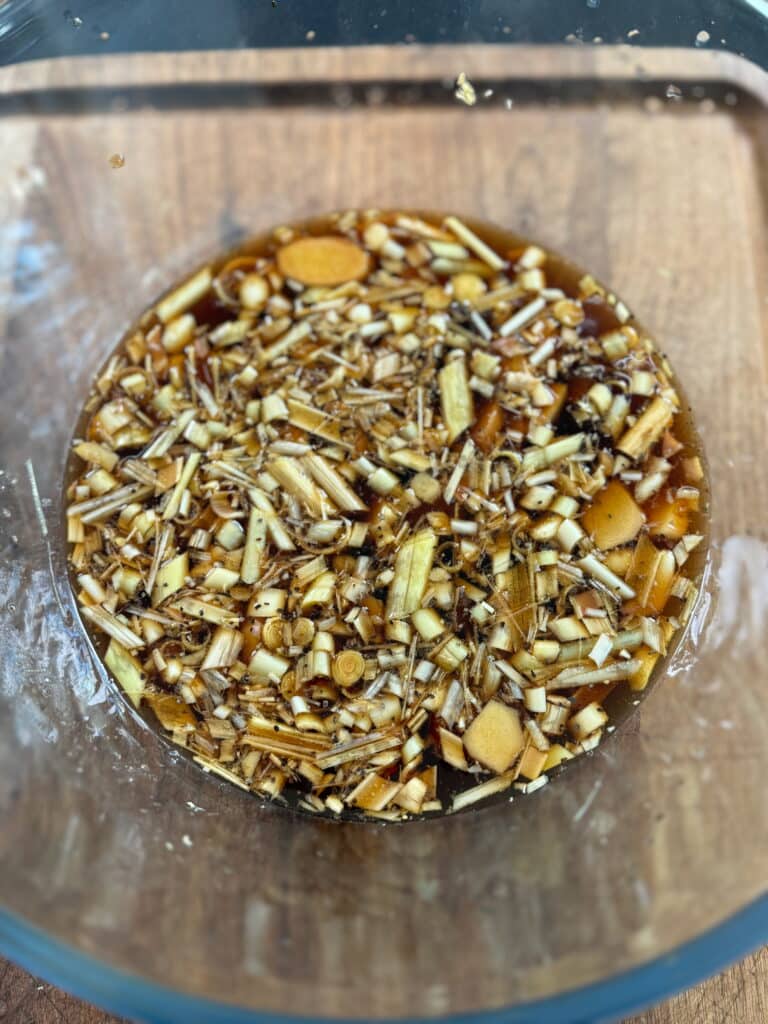 large glass bowl with chicken marinade in it with lemongrass, ginger, and garlic