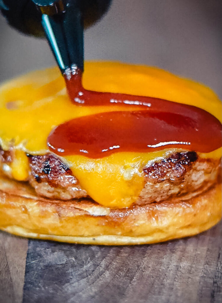 bbq sauce being drizzled onto a pork patty