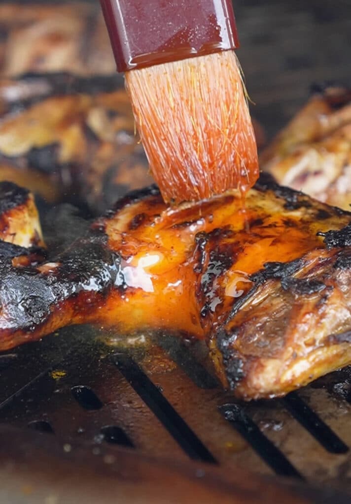 chicken on grill being basted while on a grill with flames