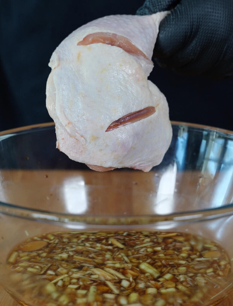 chicken quarter being placed into a bowl of marinade