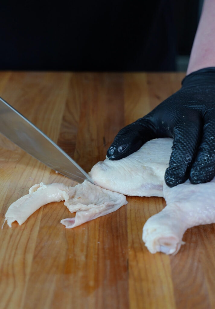 chicken skin being trimmed from a chicken thigh