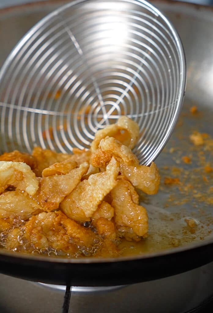 fried chicken pieces being scooped out of a frying pan