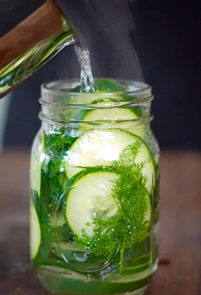 pickling liquid being poured over top of cucumbers in a glass jar