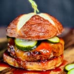 pork burger with cheddar cheese, pickles, and bbq sauce on a pretzel bun