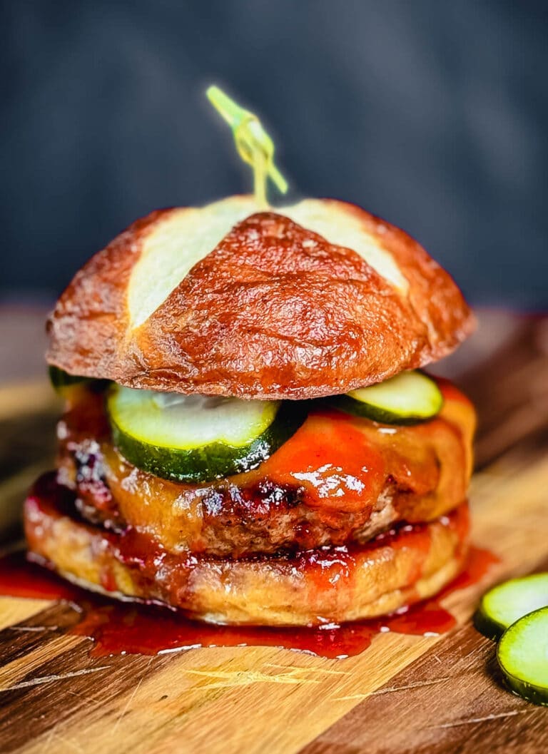 pork burger with cheddar cheese, pickles, and bbq sauce on a pretzel bun